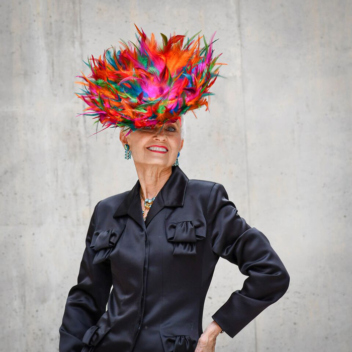 Judith in black silk outfit with colorful feathered hat | 40plusstyle.com