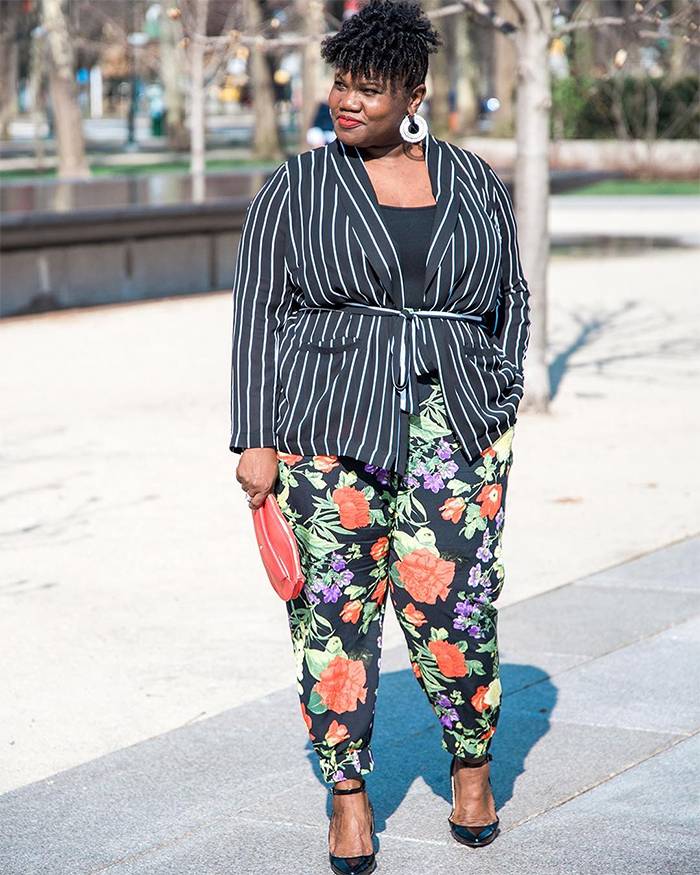 Georgette from Grown and Curvy Women is wearing Black tops over striped belted coat and floral pants with hoop earrings and red clutch | fashion over 40 | 40plusstyle